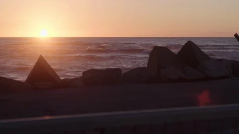 Sun setting into the sea, looking over a rock wall. Stock Footage