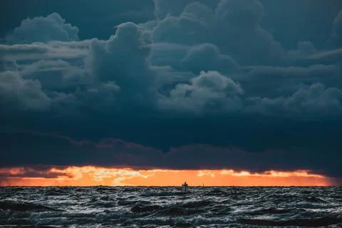 Sun setting at the sea with sailing cargo ship, scenic view. Clouds and storming Stock Photos