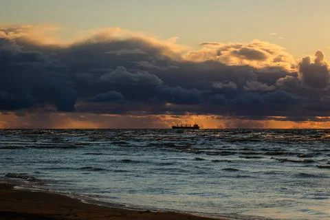 Sun setting at the sea with sailing cargo ship, scenic view. Clouds and storming Stock Photos