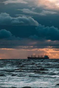 Sun setting at the sea with sailing cargo ship, scenic view. Clouds and storming Stock Photos