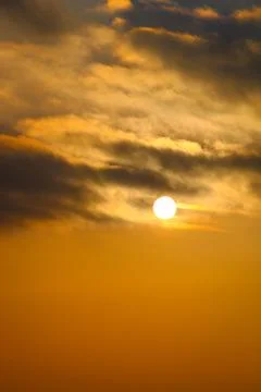 The sun is setting in the sky with the sun shining through the clouds. Stock Photos