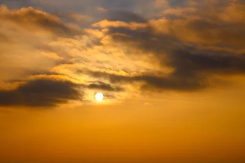 The sun is setting in the sky with the sun shining through the clouds. Stock Photos