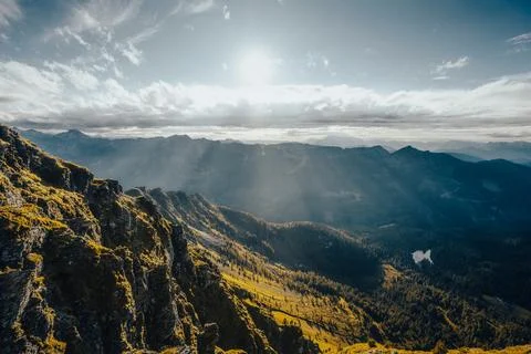 The sun shines brightly through the clouds above the mountains Stock Photos