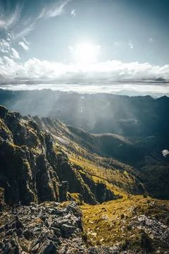The sun shines brightly through the clouds above the mountains Stock Photos