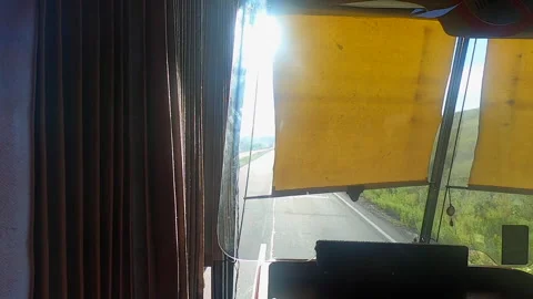 Sun shines brightly through the curtain on the driver's window of a moving bus Stock Footage 240574535