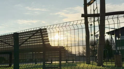 Sun Shines Over Empty Playground and Park Bench Behind Wire Fence at Sunrise Stock Footage 334513460