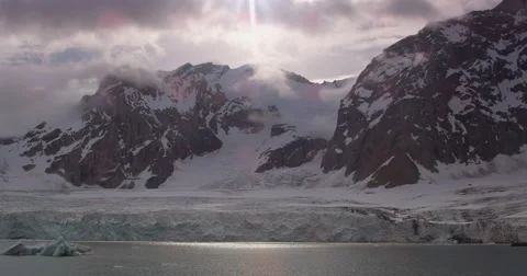 Sun shines through clouds onto icebergs in glacier fed bay Stock Footage 62023255