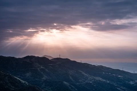 The sun shines through the clouds onto the mountain tops and the sea. Stock Photos