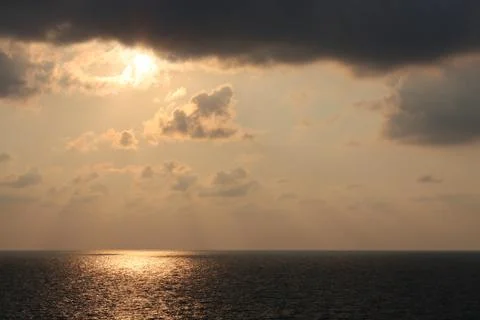 Sun shines through the clouds over sea Stock Photos