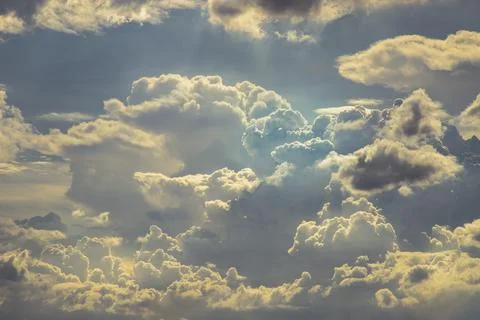 The sun shines through the clouds in the sky.  The shape of the clouds evokes Stock Photos