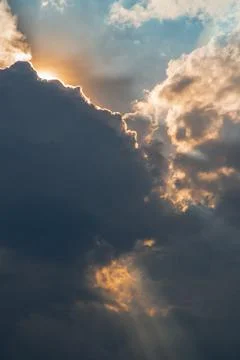 The sun shines through the clouds in the sky.  The shape of the clouds evokes Stock Photos