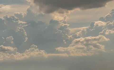 The sun shines through the clouds in the sky.  The shape of the clouds evokes Stock Photos