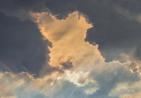 The sun shines through the clouds in the sky.  The shape of the clouds evokes Stock Photos