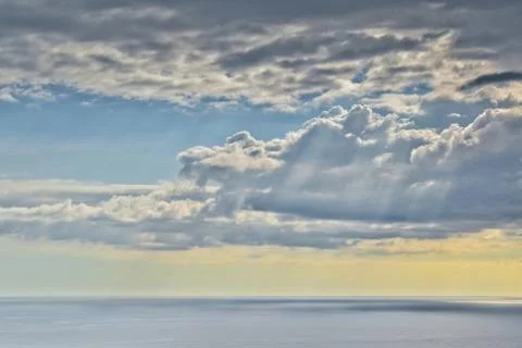 Sun shines through rain clouds over Tasman sea horizon Stock Photos