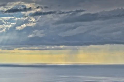 Sun shines through rain clouds over Tasman sea horizon Stock Photos