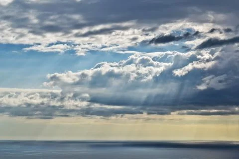 Sun shines through rain clouds over Tasman sea horizon Stock Photos