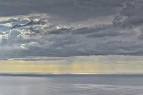 Sun shines through rain clouds over Tasman sea horizon Stock Photos