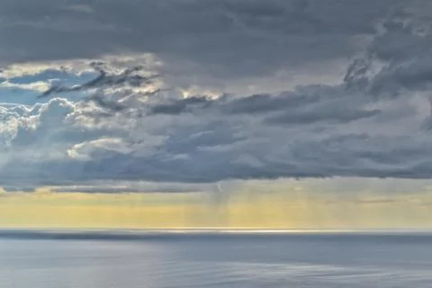 Sun shines through rain clouds over Tasman sea horizon Stock Photos