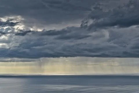 Sun shines through rain clouds over Tasman sea horizon Stock Photos