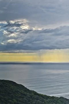 Sun shines through rain clouds over Tasman sea horizon Stock Photos