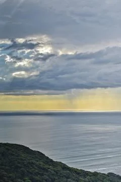 Sun shines through rain clouds over Tasman sea horizon Stock Photos