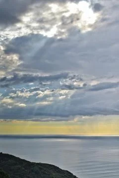 Sun shines through rain clouds over Tasman sea horizon Stock Photos