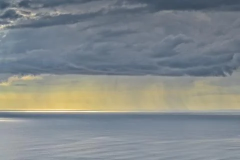 Sun shines through rain clouds over Tasman sea horizon Stock Photos