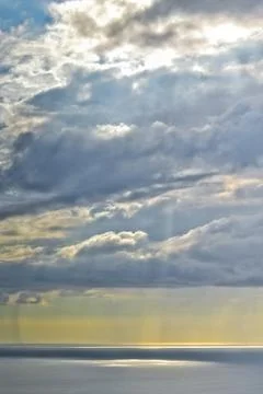 Sun shines through rain clouds over Tasman sea horizon Stock Photos