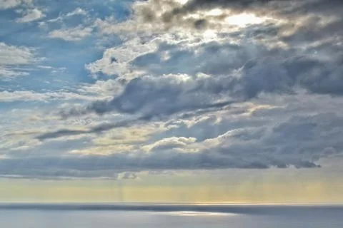 Sun shines through rain clouds over Tasman sea horizon Stock Photos