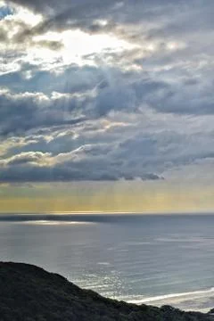 Sun shines through rain clouds over Tasman sea horizon Stock Photos