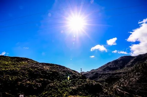 The sun is shining brightly in the sky, casting a warm glow over the mountain Stock Photos