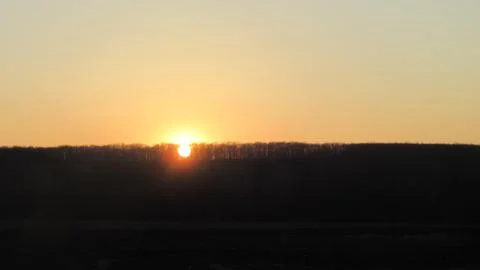 The sun, a shining disk through the trees at sunset Stock Photos