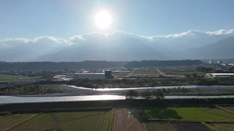 Sun Shining Over a River and Flat Farmland Below Mountains Stock Footage 347929839