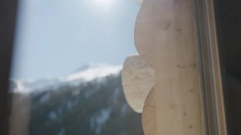 Sun shining over a snowy mountain peak, viewed from inside a rustic log cabin on Stock-Footage 334712306