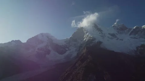 Sun shining on snowcapped mountains with clouds slowly rising from the snow  Stock Footage 252392402
