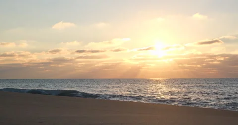Sun shining though clouds at sunset on empty beach with rays of light Stock Footage 146669273