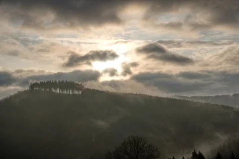 Sun shining through the clouds in the mountains with fog on the hill Stock Photos