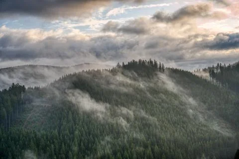 Sun shining through the clouds in the mountains with fog on the hill Stock Photos