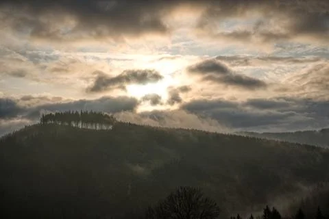 Sun shining through the clouds in the mountains with fog on the hill Stock Photos