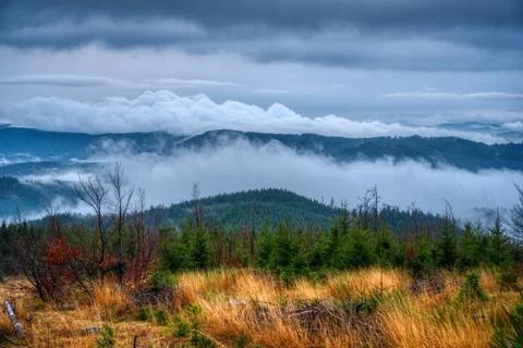 Sun shining through the clouds in the mountains with fog on the hill Stock Photos