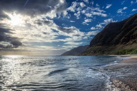 Sun shining through the clouds at sandy beach with waves Stock Photos