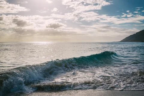 Sun shining through the clouds at sandy beach with waves Stock Photos