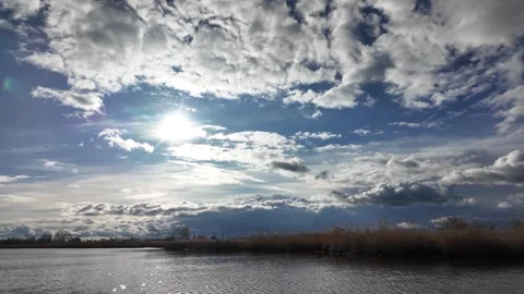 Sun shining through dramatic clouds above a calm lake and reeds Stockbeeldmateriaal 348263786