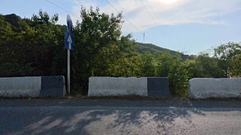 Sun shining through trees near jersey barrier on a rural road Vidéo 311403141