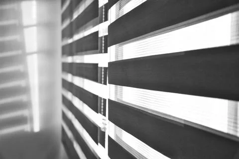Sun shining through window blinds throwing shadows on the wall in black and w Stock Photos