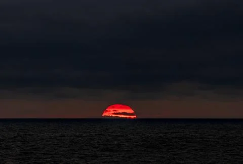 The sun is slowly setting over the vast ocean under a cloudy sky Stock Photos