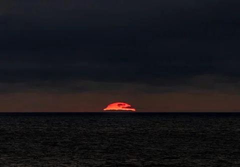 The sun is slowly setting over the vast ocean under a cloudy sky Foto stock