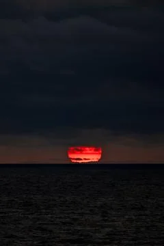 The sun is slowly setting over the vast ocean under a cloudy sky Stock Photos