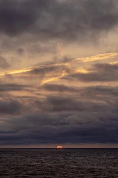 The sun is slowly setting over the vast ocean under a cloudy sky Stock Photos