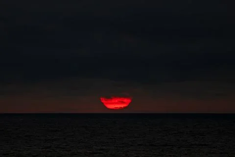 The sun is slowly setting over the vast ocean under a cloudy sky Stock Photos
